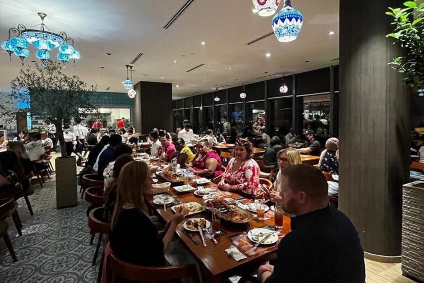 A long shared table at Sofra set for a large group under mosaic lanterns